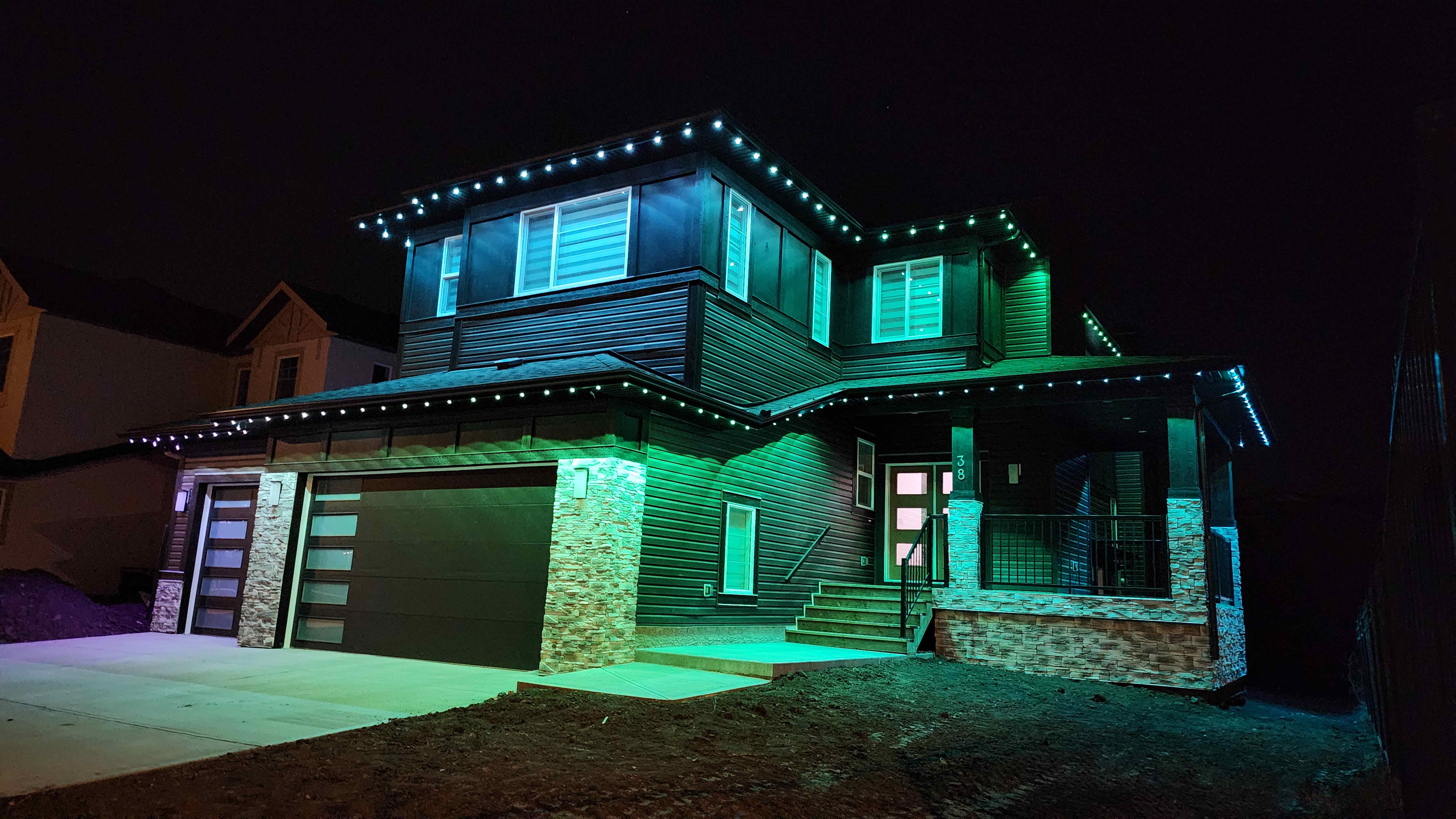 Large home lit entirely in green and teal along the eaves and porch