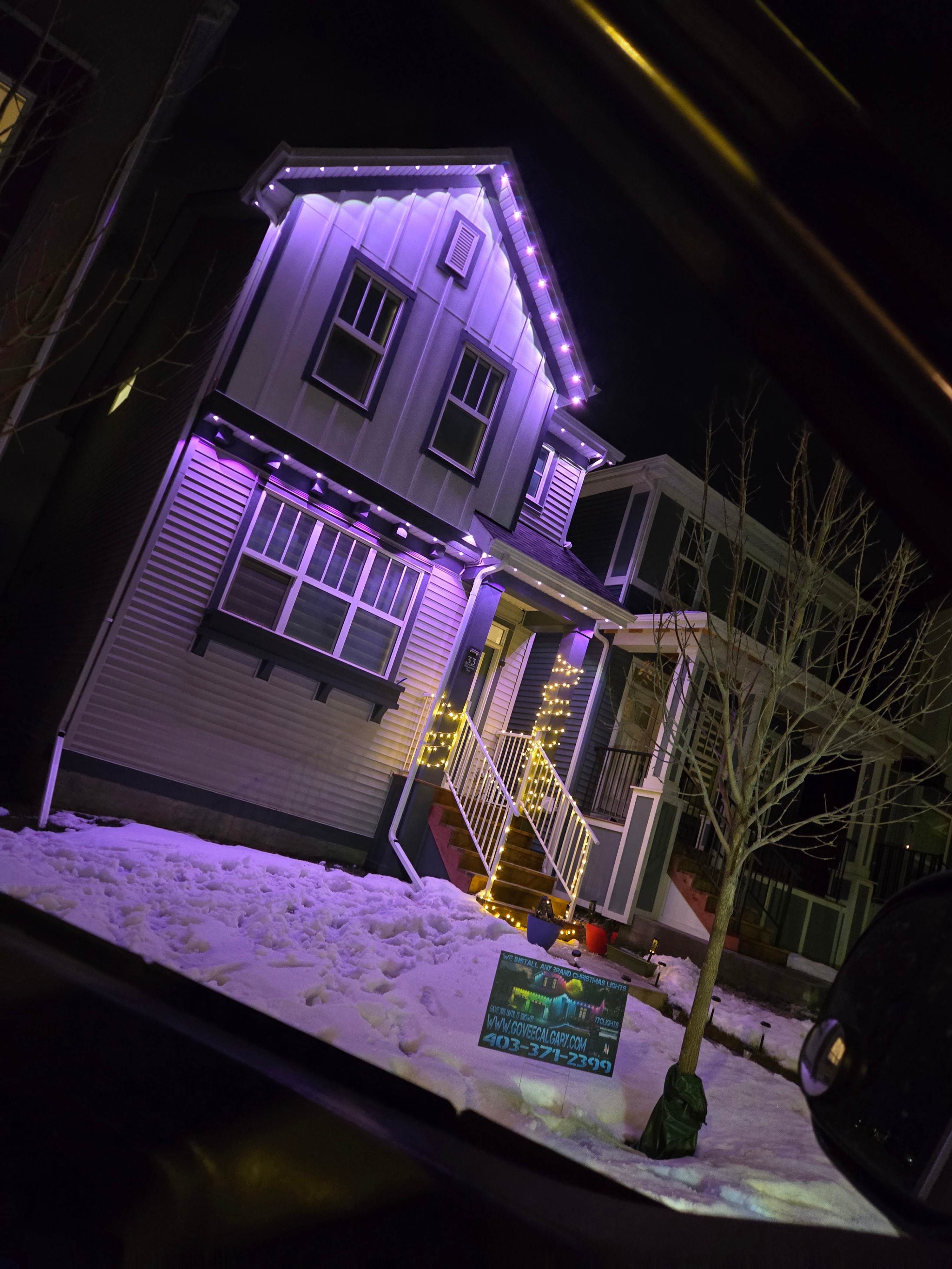Home glowing purple at dusk with a Govee Calgary yard sign in the snow